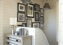 Beachy cottage foyer entry design with gray washed vintage chest, tapered cone metal pendants, off-white wood paneling and eclectic photo wall gallery.