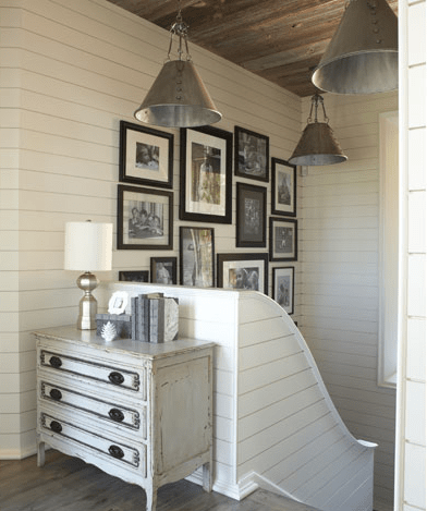 Beachy cottage foyer entry design with gray washed vintage chest, tapered cone metal pendants, off-white wood paneling and eclectic photo wall gallery.