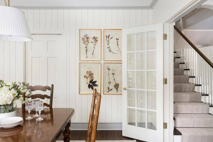 Stacked vintage botanical prints hang from vertical shiplap trim in a charming cottage dining space.