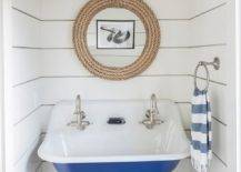 Small white and blue beach style boys' bathroom boasts a woven towel basket placed beneath a blue Kohler Brockway Sink finished with stain nickel vintage style faucets. The sink is mounted to a white tongue and groove wall under a round rope mirror hung between nickel and white glass sconces.