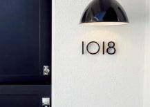 Modern black house numbers illuminated with a glossy black industrial sconce beside a black dutch door with a chrome door handle.