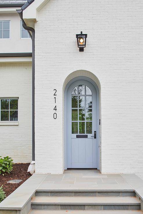 Slate steps lead to slate pavers located in front of a blue plank arch front door positioned beside modern vertical house numbers and beneath a glass and oil rubbed bronze lantern.