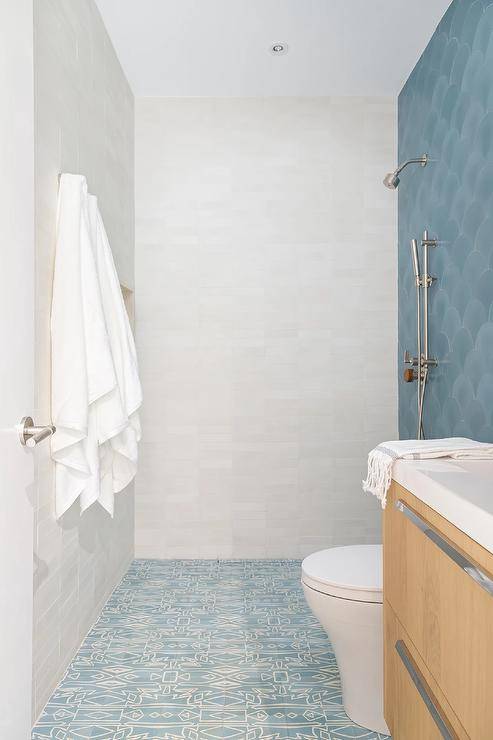 Small bathroom features white and blue mosaic floor tiles leading past a tan oak washstand and a white porcelain toilet to an open shower accented with blue scale wall tiles.