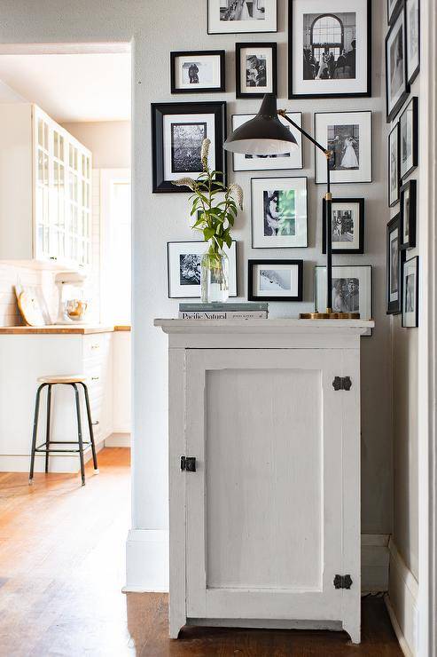Aerin Charlton Lamp adorns a white painted vintage foyer cabinet styled with a black and white photo gallery wall in a small foyer space.