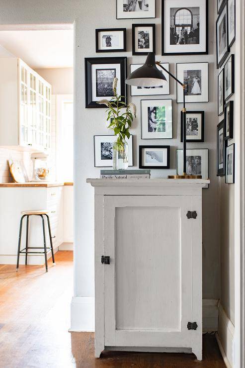 Aerin Charlton Lamp adorns a white painted vintage foyer cabinet styled with a black and white photo collage wall in a small foyer space.