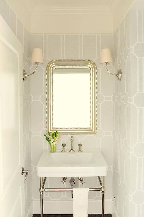 Clad in gray geometric wallpaper, this small chic powder room features a silver leaf beaded French mirror hung between facing Vendome Single Sconces and over a nickel and porcelain sink vanity.