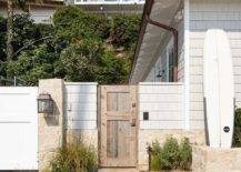 Rustic stone pavers lead to a salvaged wood gate accenting a light gray shingled beach cottage home.