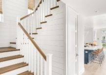 Cottage foyer and stairs featuring a tan staircase handrail with white wooden balusters finished with a shiplap wall and a closet under the staircase.