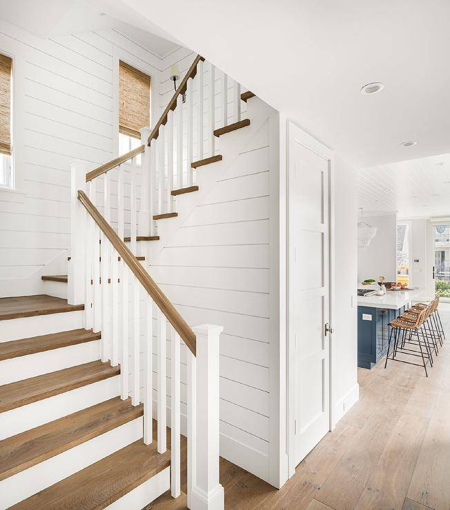 Cottage foyer and stairs featuring a tan staircase handrail with white wooden balusters finished with a shiplap wall and a closet under the staircase.