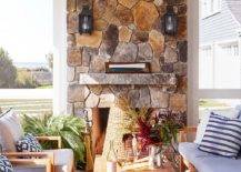 Gorgeous cottage sunroom features a stunning stone fireplace fitted with carriage sconces mounted over a stone mantel.