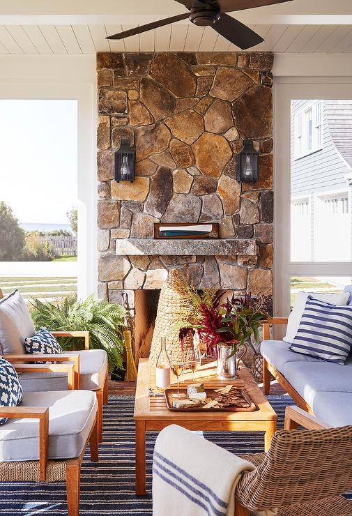Gorgeous cottage sunroom features a stunning stone fireplace fitted with carriage sconces mounted over a stone mantel.