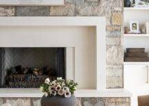 A white, black, and gray abstract art piece hangs from a gray stone fireplace wall over a white mantel finished with a gray stone hearth and gray brick herringbone firebox.