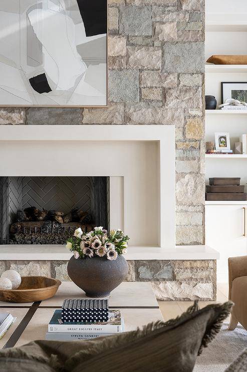 A white, black, and gray abstract art piece hangs from a gray stone fireplace wall over a white mantel finished with a gray stone hearth and gray brick herringbone firebox.