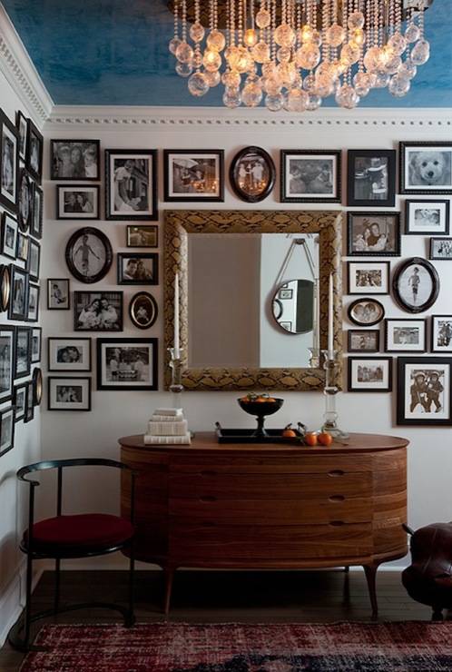 Stunning foyer with eclectic black & white photo gallery, faux python mirror, vintage oval console table, red & blue wool rug and crystal drops chandelier.