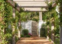An ivy wrapped pergola leads to a brown wooden door.