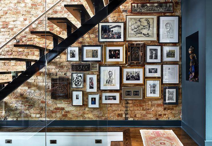 Eclectic foyer boasting a floating-style staircase and an exposed brick wall finished with gallery wall art in various placements and frames.