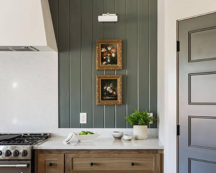 Cottage kitchen features hunter green vertical shiplap backsplash over light brown cabinets topped with white marble.