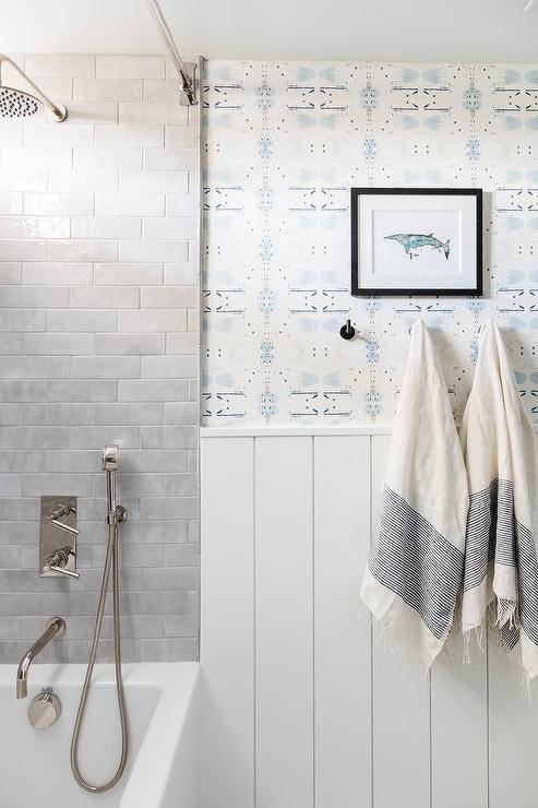White and blue wallpaper is accented with white vertical shiplap trim, as a smal blue art piece hangs over oil rubbed bronze towel hooks.