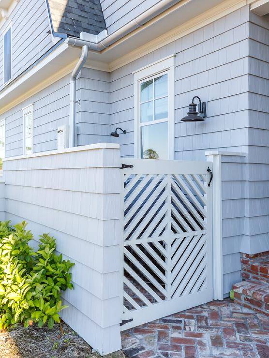 This lovely gray shingled home is accented with red brick herringbone pavers leading throw a white wooden gate.