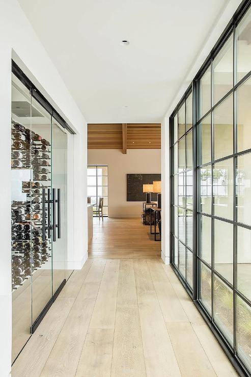 A long hallway with a wide plank wood floor boasts a glass wine cellar fitted with vertical wine racks.