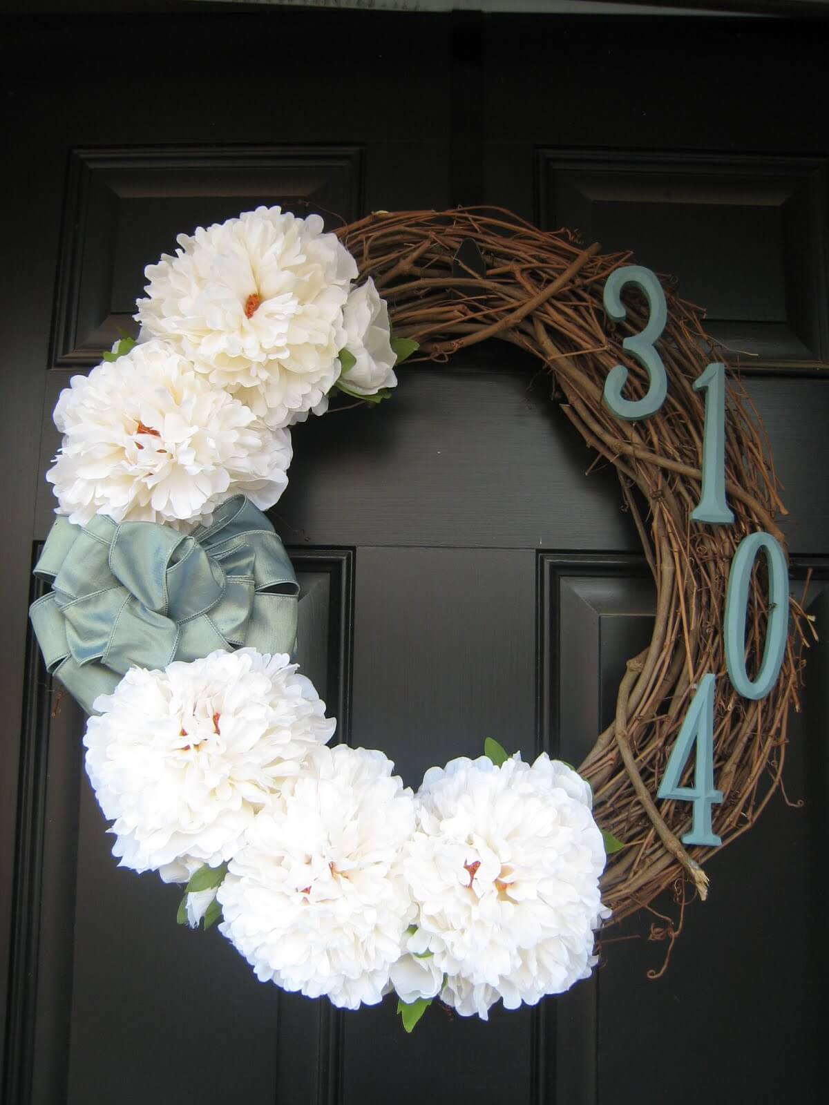 close up of wreath on front door with house numbers and white flowers blue ribbon