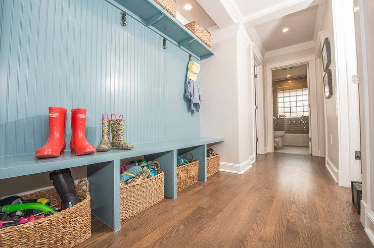 Long blue built-in mudroom bench with blue beadboard trim features woven baskets for extra storage accessible for the entire family.