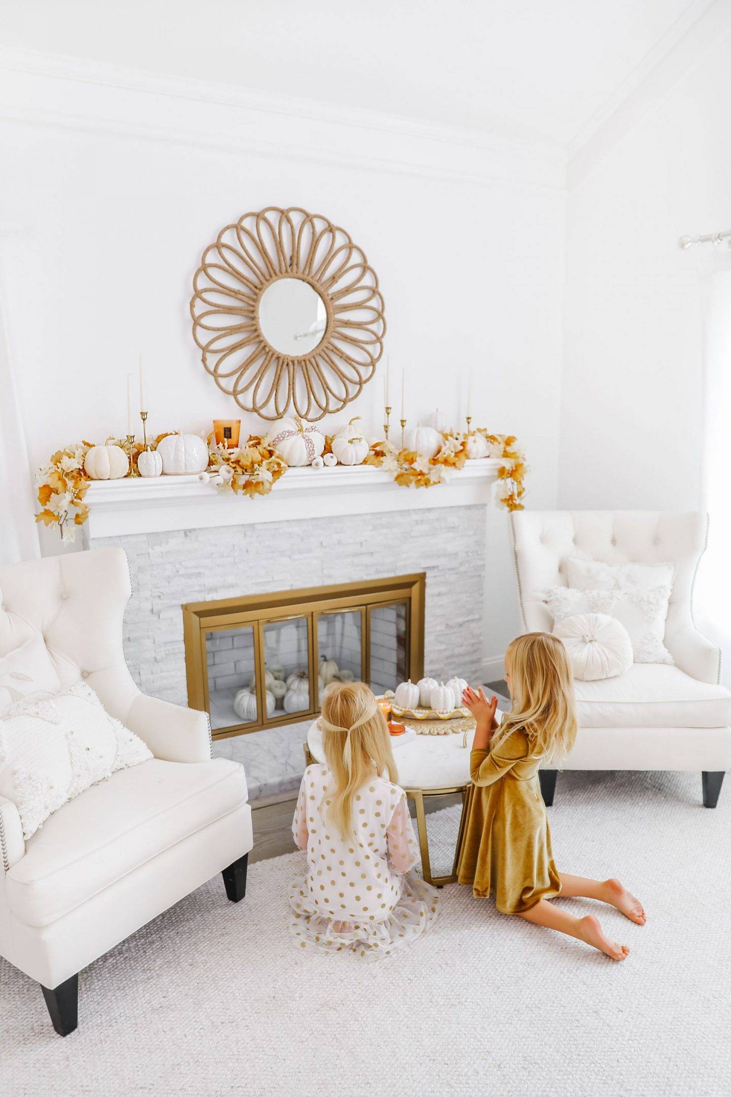 Two kids in front of a neutral fireplace mantel with subtle fall decor.