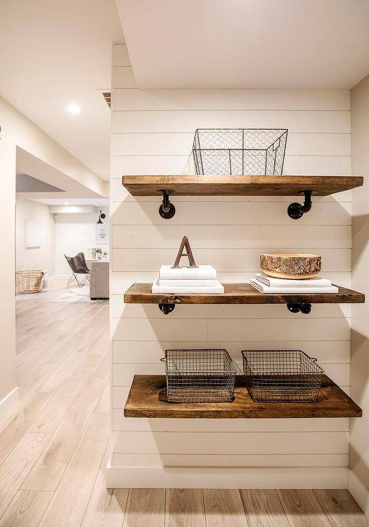 Industrial wood and pipe plumbing shelves are styled and stacked against a shiplap wall.