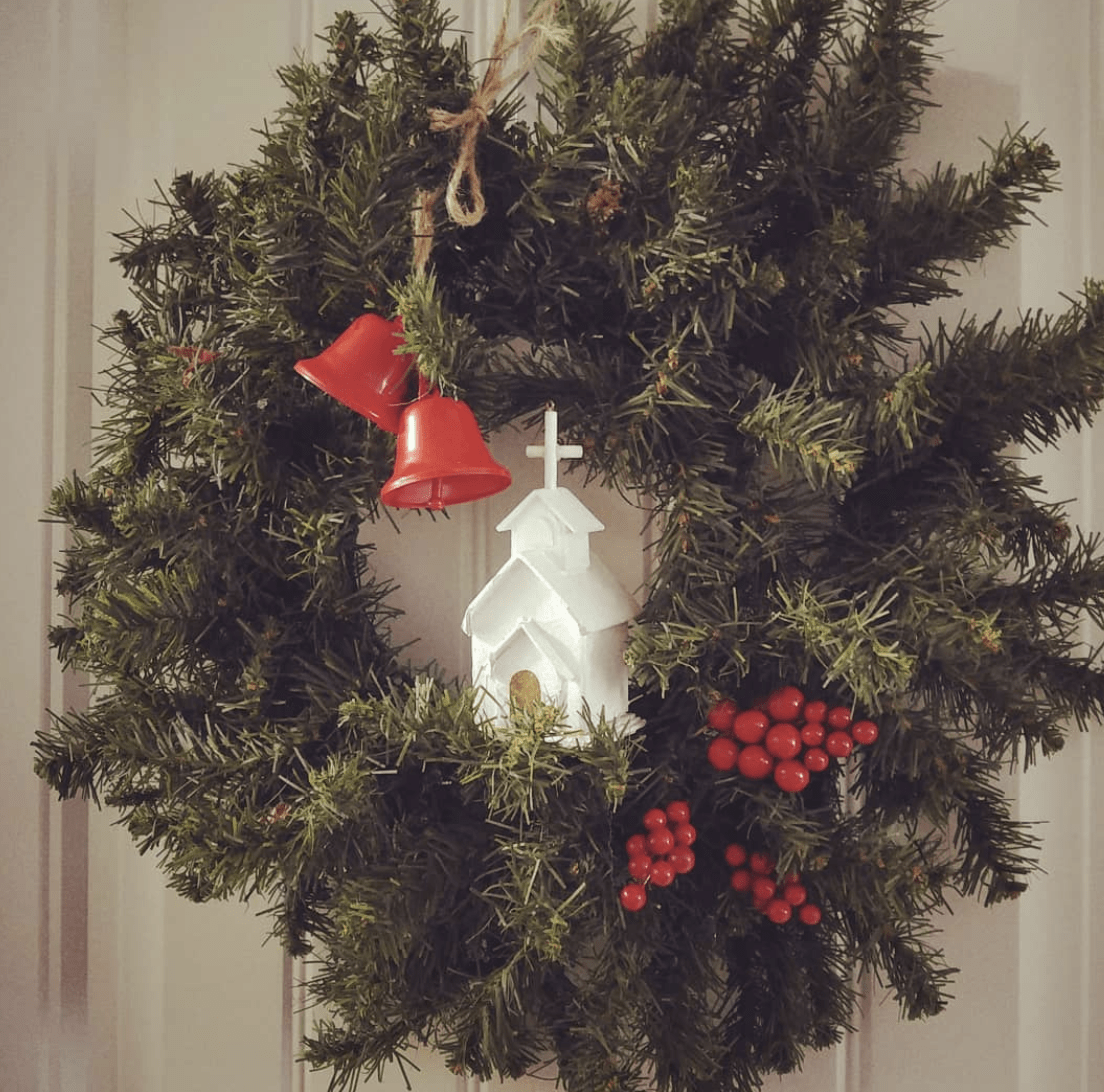 evergreen wreath with two small ornaments white church and red bells