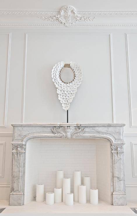 French living room features walls clad in decorative wall moldings and ornate beaded crown moldings lined with a French marble fireplace filled with candles.