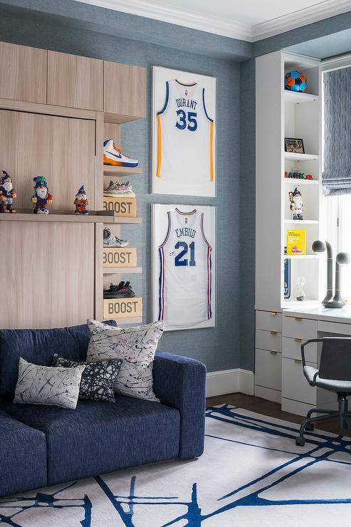 Basketball themed home office features framed jerseys on blue textured wallpaper and a blue couch on a white and blue rug.