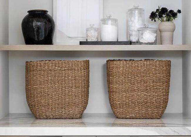 Bathroom features styled gray veneer linen shelves and cabinets with brown woven baskets.