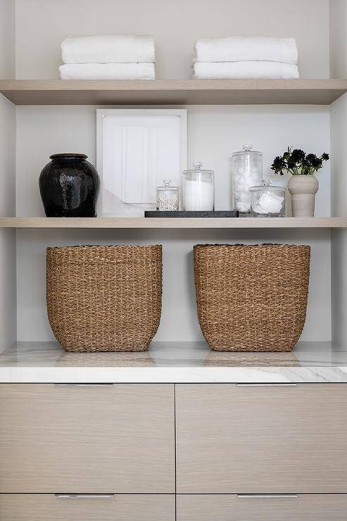 Bathroom features styled gray veneer linen shelves and cabinets with brown woven baskets.