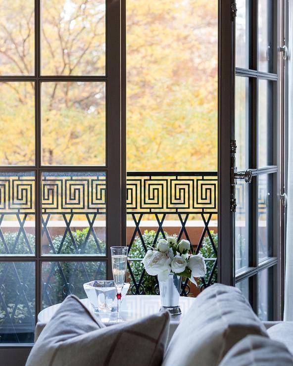 Black French doors with vintage French casement hardware open to a patio accented with Greek key balcony trim.