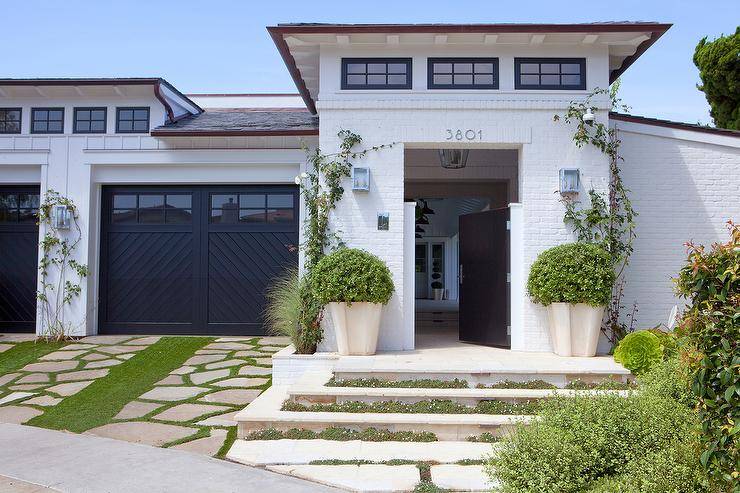 White brick home is accented with a black front door with an attached garage with black chevron doors.