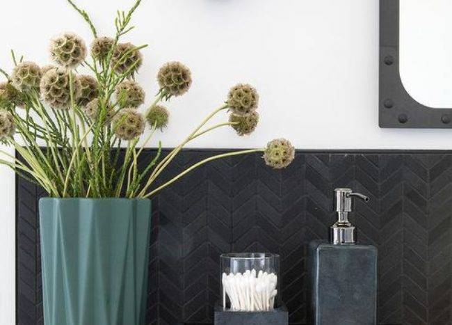 In this vanity area, dark backsplash suggests an updated contemporary influence. Matte black chevron pattern backsplash tiles accents continue a black and white scheme with styled decor. A 3-inch edge white quartz countertop finishes a single washstand providing a contemporary counterpoint.