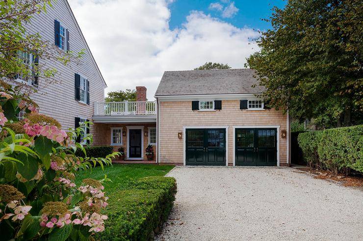 Shake shingled siding garage with two doors designed in a cottage home with stunning curb appeal from a gravel driveway to the lovely green landscape.