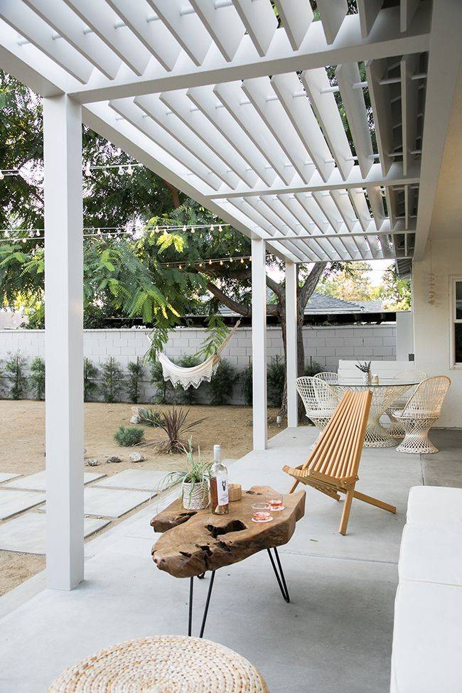 white boho pergola on concrete patio with bamboo teak chair wood log slice coffee table