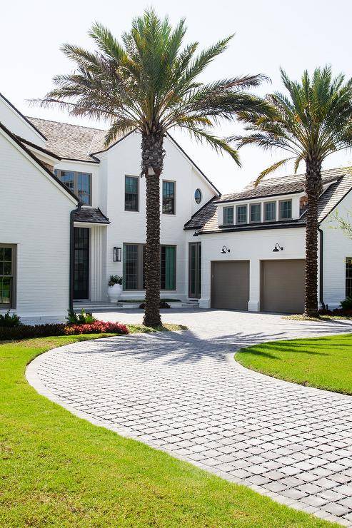 White beach house features gray brick winding driveway that leads to a 2-car attached brown garage.