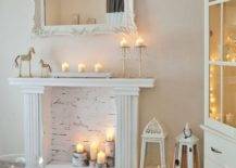 a faux white fireplace with candles placed on tree stumps, with candle lanterns and candles on the mantel