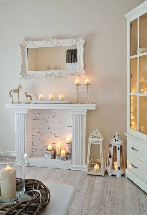 a faux white fireplace with candles placed on tree stumps, with candle lanterns and candles on the mantel