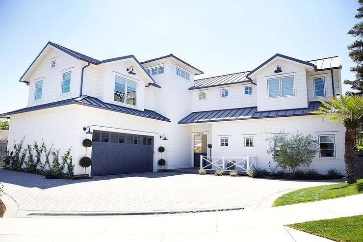 White and blue home with a blue garage door displaying topiaries and black vintage lamps on the sides. Navy roofing and white siding invite a modern farmhouse appeal to the home design.