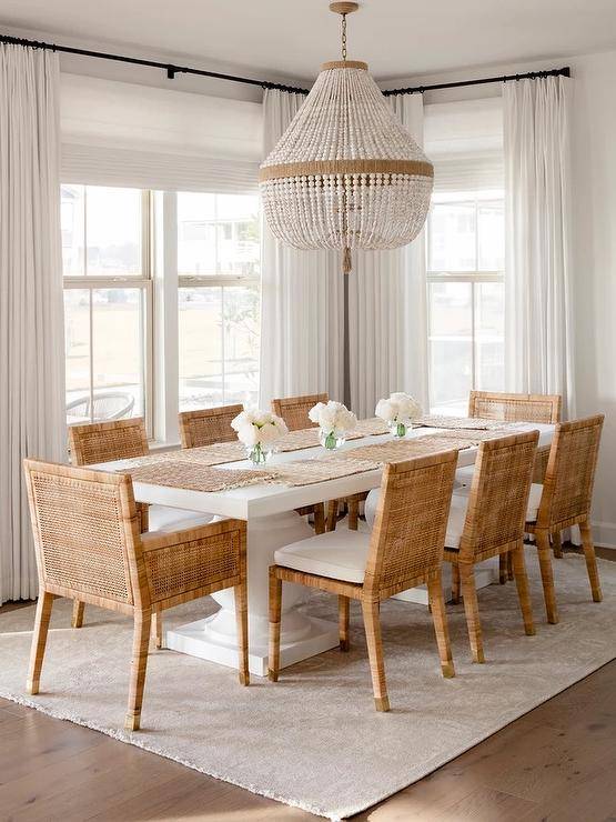 Elegant dining room features an ivory beaded chandelier that illuminates Serena & Lily balboa chairs at a Serena & Lily terrace dining table atop a tan rug and cream curtains.