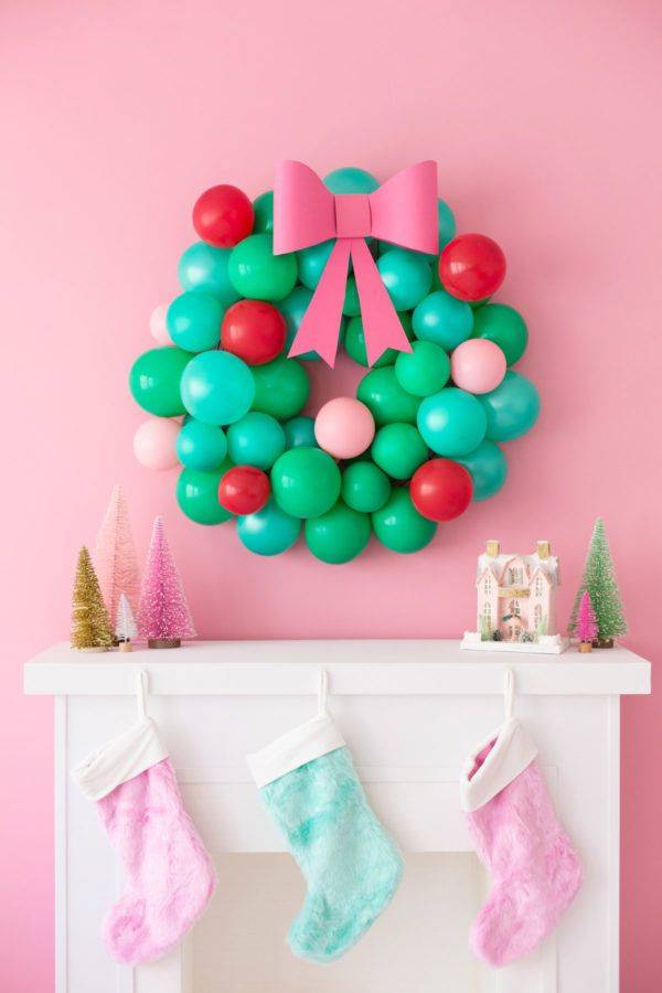 colorful green red and pink balloons made into christmas wreath pink ribbon on white fireplace