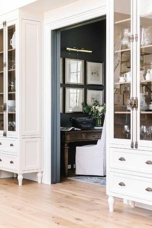 Cottage style home office with gray pocket doors features a brown farmhouse desk with white slipper chair.