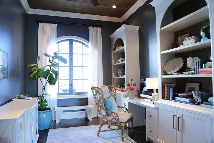 Cottage style home office features a bamboo wingback Chippendale chair at a marble top white built-in desk with white built-in shelves on black walls and white curtains.