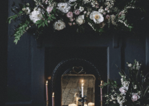 dark and moody fireplace with floral arrangements and white lit candles inside completely black