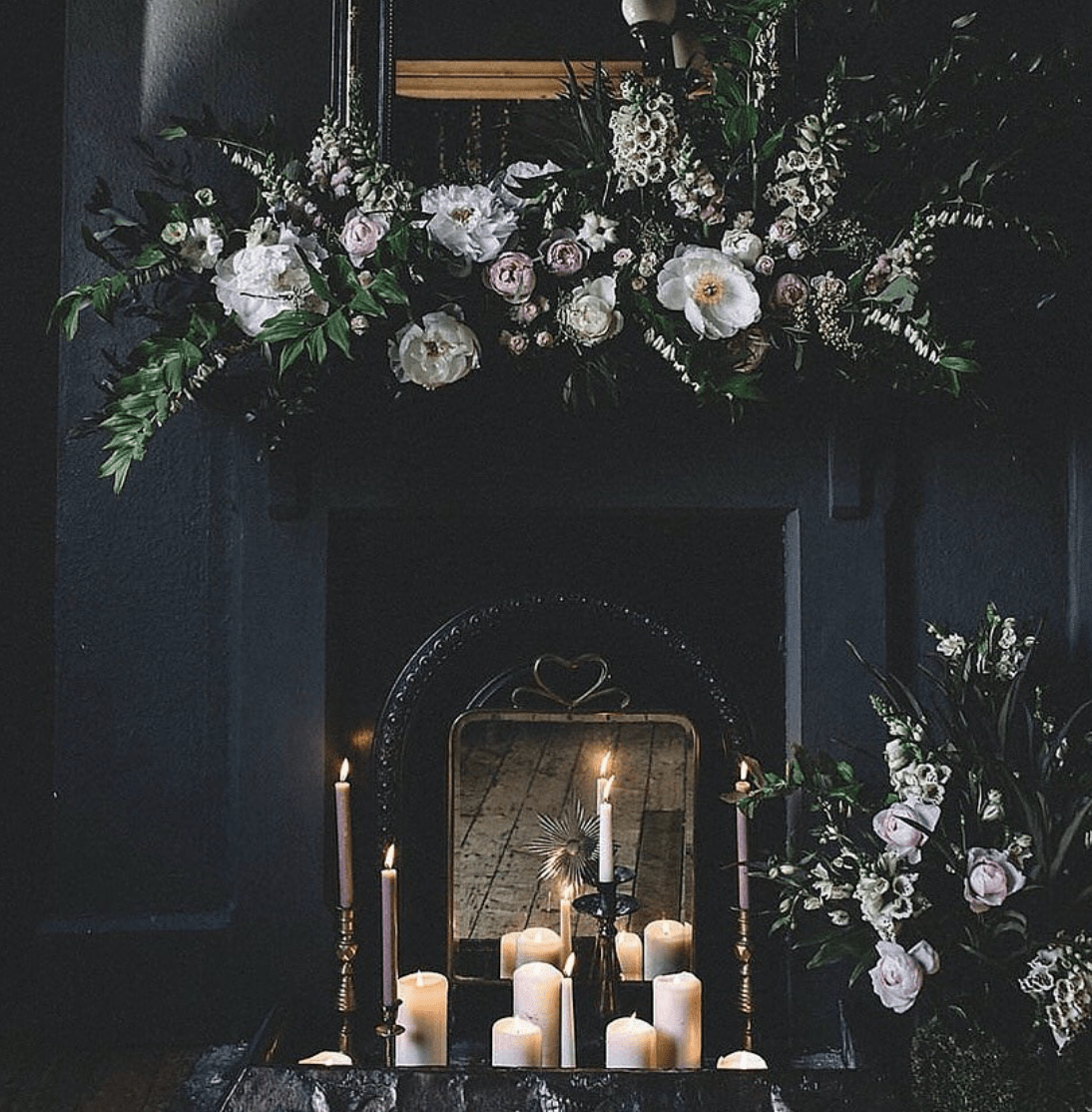 dark and moody fireplace with floral arrangements and white lit candles inside completely black