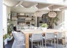 Gray rope dining chairs surround a teak outdoor dining table placed beneath a pergola.