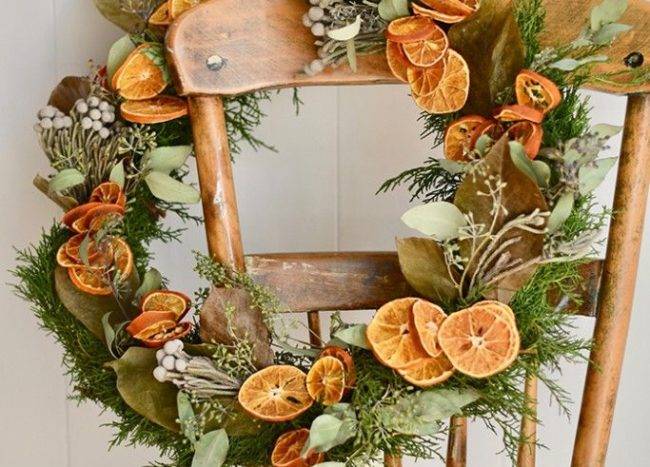 Natural, real greenery Christmas wreath with dried oranges hanging on vintage chair white background